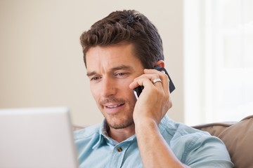 Smiling man using laptop and mobile phone in living room