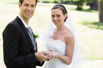 Groom placing ring on brides finger at park