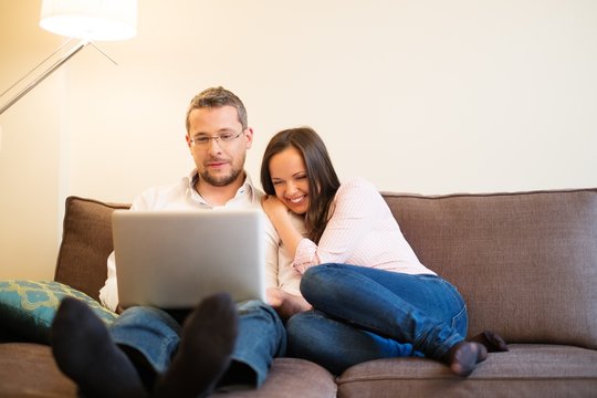 Young cheerful couple with laptop on a sofa in home interior
