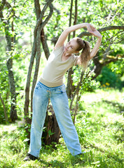 The young slender woman does sporting training in park 