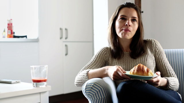 Young woman eating croissant and drinking juice at home