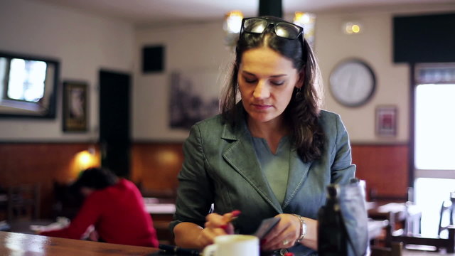 Businesswoman using lipstick in cafe looking on cellphone, stead