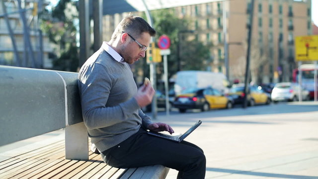 Man finishing work on a laptop and eating croissant on street be