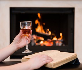 hands holding glass of cognac and book by the fireplace