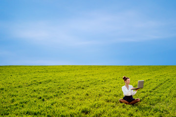 Naklejka na ściany i meble Young woman, girl working with laptop in green field with blue s