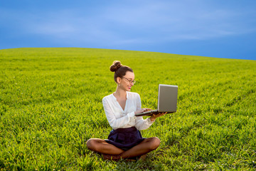 Young woman, girl working with laptop in green field, park with