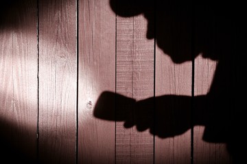 Unrecognizable burglar with  flashlight  in shadow on wood backg