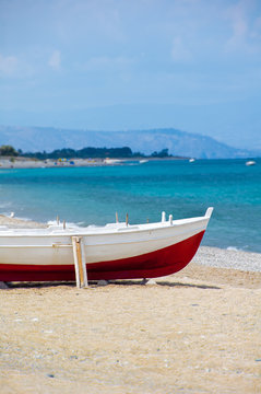 A red and white wooden boat on a beach in the south of Italy