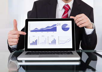 Confident Businessman Displaying Laptop At Desk
