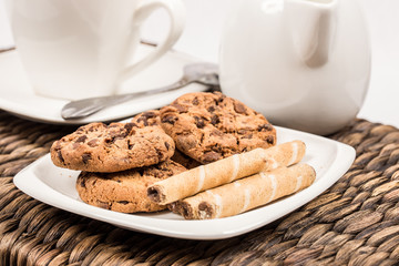 chocolate cookies with wafer rolls next to cup of coffee