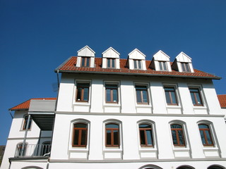 Weiße sanierte ehemalige Zigarrenfabrik mit Dachgauben und Mansarden vor blauem Himmel im...