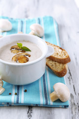 Mushroom soup in white pot, on napkin,  on wooden background