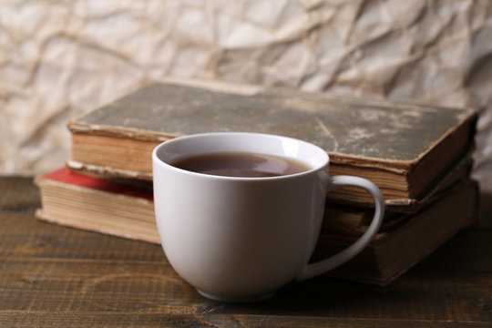 Cup of hot tea with books on table on paper background
