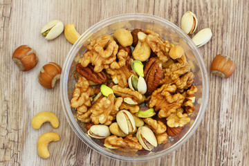 Selection of mixed nuts in plastic box on wooden surface