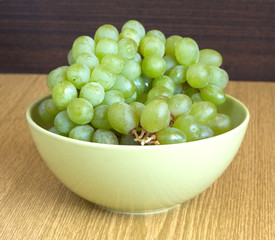 Grape on branch in green bowl on sandy brown wooden table