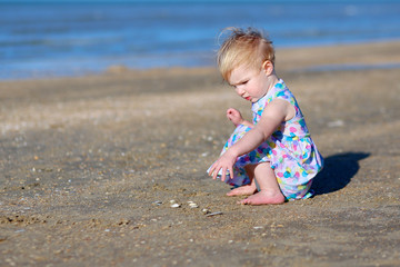 Cute toddler girl playing on the beach on summer day