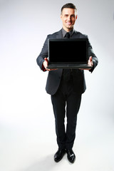 Happy businessman standing with laptop on gray background
