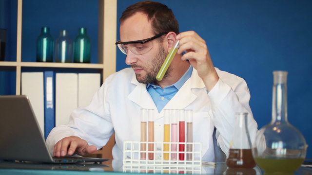 Scientist examine chemicals in test tubes, writing results on la