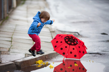 Little boy with umbrella, jumping in muddy puddles