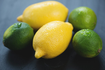 Ripe lemons and limes over black wooden background, close-up