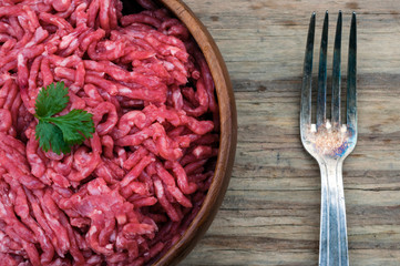 bowl of raw mince meat and fork on a wooden background