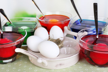 Eggs with liquid colour in glass on table on bright background