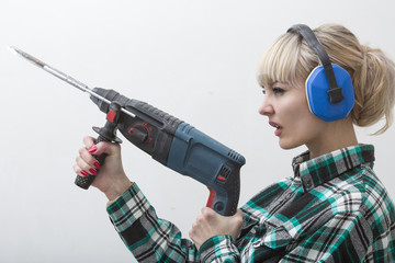 Woman in earphones holds construction tool, puncher in hand.