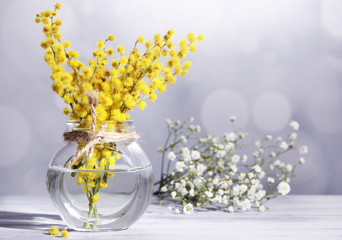 Twigs of mimosa flowers in vase on wooden table