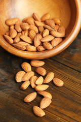 Almonds in bowl on color wooden background
