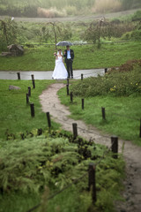 Photo of newlyweds walking on hills at rainy day