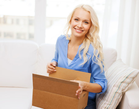 smiling young woman opening cardboard box at home
