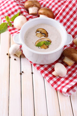 Mushroom soup in white pot, on napkin, on wooden background