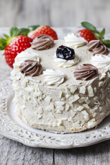 Round vanilla cake on cake stand. Fresh strawberries in the back