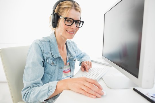 Blonde designer wearing headphones working at computer smiling a