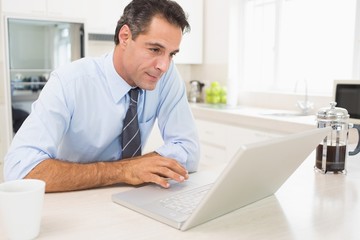 Fototapeta premium Concentrated well dressed man using laptop in kitchen