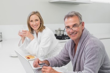 Obraz premium Happy couple in bathrobe doing online shopping at home