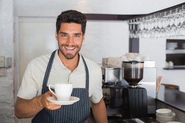 Smiling male barista holding cup of coffee at café