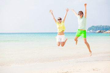 Young couple in bright clothes jumping on the beach