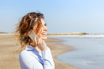 Smiling young woman talking on the mobile phone at the seaside