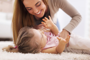 Loving mother playing with little girl on carpet