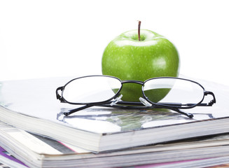 green apple and glasses on magazine and  book stack close up
