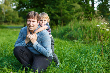 Fototapeta premium Little boy and his father sitting on grass in summer forest
