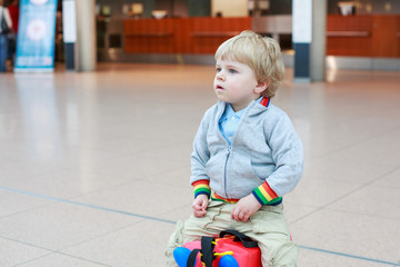 Funny toddler boy going on vacations trip with suitcase at airpo