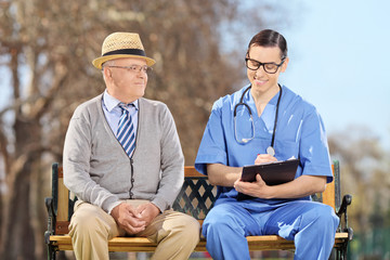 Naklejka na ściany i meble An elderly and a doctor sitting in park
