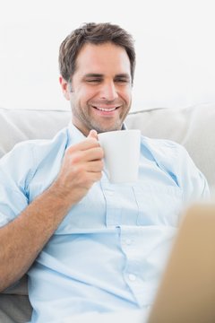 Smiling man using laptop sitting on sofa having a coffee
