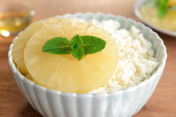 Bowl of tasty cottage cheese with pineapple on wooden table