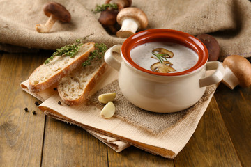 Mushroom soup in pot, on wooden background