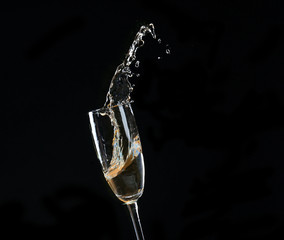 Glass of champagne with splash, on black background