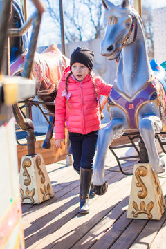 Little funny girl on carousel at an amusement park