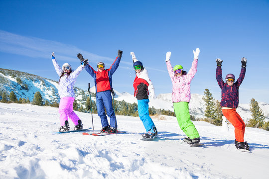 Skier and snowboarders in a row lifting hands up